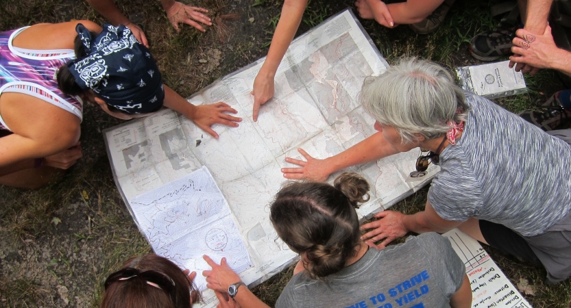 a group of people examine a map that is spread out on the ground